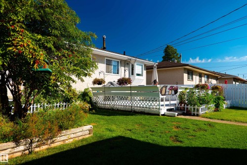 Expansive grass lawn, wood-finish retaining wall, mature deciduous tree, white picket fence, and white lattice deck surround - 11119 137 Avenue Nw, Edmonton, AB 