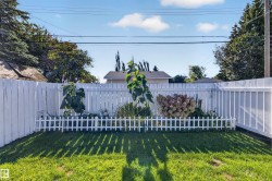 Expansive lawn area with a white privacy fence and decorative garden bed - 