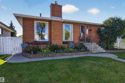 Brick exterior with prominent chimney, front entry with wrought iron railing, concrete steps, and a decorative front door - 