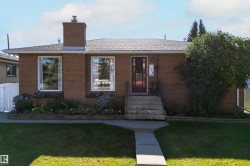 Brick exterior with a prominent brick chimney, concrete walkway, and established landscaping - 