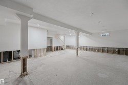 Expansive lower-level space with concrete flooring, recessed lighting, support columns, and partially finished walls - 