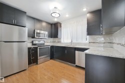 Kitchen featuring dark-toned cabinetry, stainless steel appliances, light-toned countertops, tile backsplash, and wood-finish flooring - 