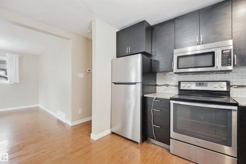 Kitchen featuring dark cabinetry, stainless steel appliances, a white subway tile backsplash, and light-toned countertops - 13420 117 Avenue Nw, Edmonton, AB 