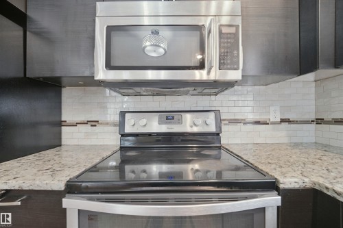 Stainless steel microwave, stainless steel range with ceramic cooktop, white subway tile backsplash with decorative accent, and light-toned countertop - 13420 117 Avenue Nw, Edmonton, AB 