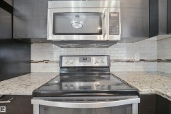 Stainless steel microwave, stainless steel range with ceramic cooktop, white subway tile backsplash with decorative accent, and light-toned countertop - 