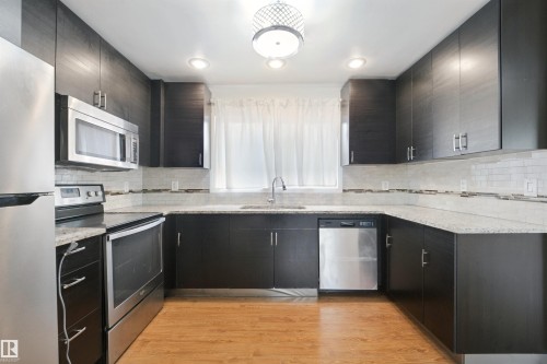 U-shaped kitchen with dark wood-finish cabinetry, light-toned countertops, and stainless steel appliances - 13420 117 Avenue Nw, Edmonton, AB 