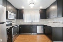 U-shaped kitchen with dark wood-finish cabinetry, light-toned countertops, and stainless steel appliances - 