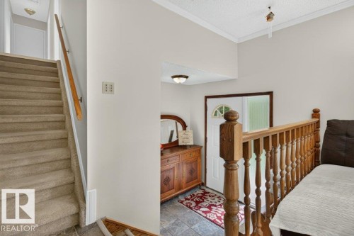 Entryway featuring a white paneled door with an arched glass insert, tiled flooring, wood-finish balusters, and a carpeted staircase - #74 22555 Twp Road 530, Rural Strathcona County, AB 