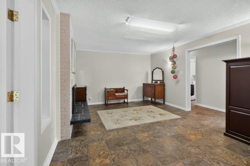 Spacious room featuring tile flooring, crown molding, and a light brick fireplace with a dark stone hearth - #74 22555 Twp Road 530, Rural Strathcona County, AB 