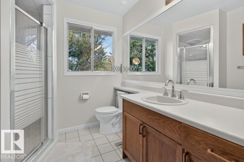 White tile flooring, wood-finish vanity with a single basin sink, large mirror, glass-enclosed shower, and a window - #74 22555 Twp Road 530, Rural Strathcona County, AB 