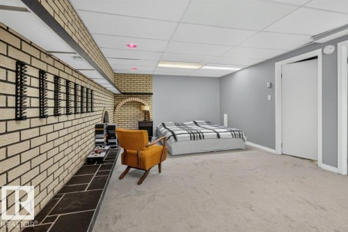Brick accent wall, stone-look hearth, drop ceiling, light-colored carpeting, and painted walls - #74 22555 Twp Road 530, Rural Strathcona County, AB 