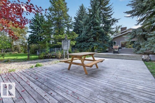 Expansive wood-finish deck with a built-in privacy fence, surrounded by mature trees and lush greenery - #74 22555 Twp Road 530, Rural Strathcona County, AB 