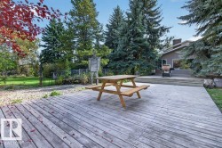 Expansive wood-finish deck with a built-in privacy fence, surrounded by mature trees and lush greenery - 