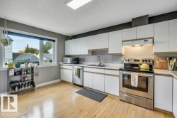 Kitchen featuring light wood-finish flooring, white cabinetry, stainless steel appliances, white countertops, and a window with a roller blind - 