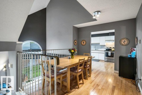 Hardwood flooring, open concept dining area, semi-open kitchen with stainless steel appliances, upper railing, and an arched window - #24 3811 85 St Nw, Edmonton, AB 