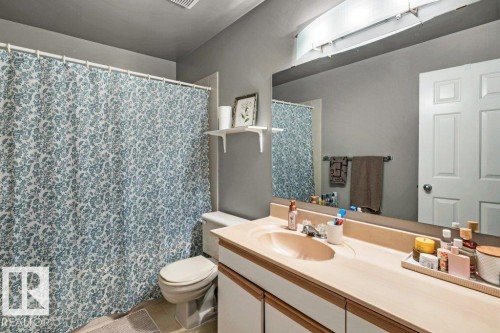 Bathroom featuring a single vanity with an integrated sink, full-width mirror, overhead lighting, and a white paneled door - #24 3811 85 St Nw, Edmonton, AB 