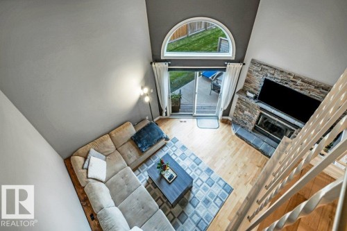 Vaulted ceiling with an arched transom window, wood-finish flooring, a stone-clad fireplace, and sliding glass doors to the exterior - #24 3811 85 St Nw, Edmonton, AB 