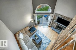 Vaulted ceiling with an arched transom window, wood-finish flooring, a stone-clad fireplace, and sliding glass doors to the exterior - 
