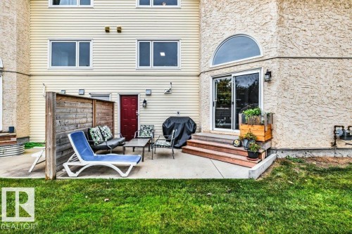 Rear exterior featuring a concrete patio, wood privacy screen, sliding glass door, arched window, and two-story siding and stucco facade - #24 3811 85 St Nw, Edmonton, AB 