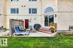 Rear exterior featuring a concrete patio, wood privacy screen, sliding glass door, arched window, and two-story siding and stucco facade - 