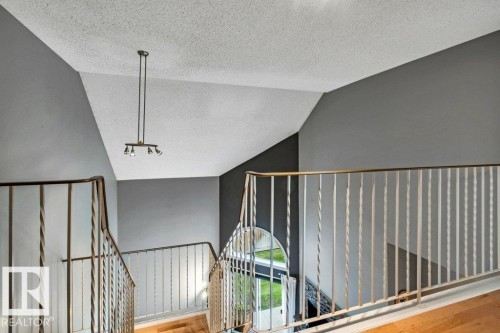 Vaulted ceiling with track lighting, metal baluster railing, wood-finish flooring, and an arched window - #24 3811 85 St Nw, Edmonton, AB 