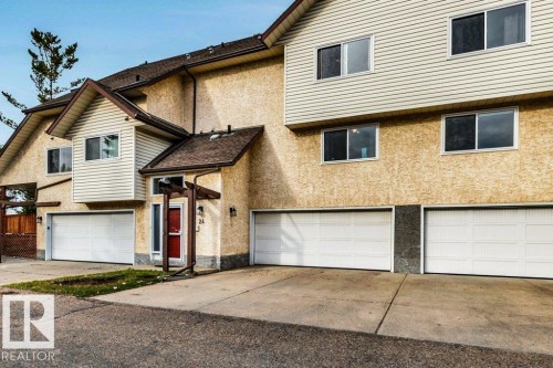 Multi-level townhouse with stucco and siding exterior, multiple garage doors, and individual entry with a red door - #24 3811 85 St Nw, Edmonton, AB 