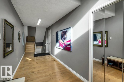 Wood-finish flooring, staircase with wood treads, mirrored sliding closet doors, and light gray wall paint - #24 3811 85 St Nw, Edmonton, AB 