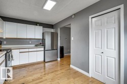 Wood-finish flooring, white cabinetry, stainless steel refrigerator, and recessed ceiling lighting - 