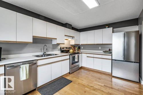 Kitchen featuring white cabinetry, light wood-finish flooring, stainless steel appliances, white countertops, and a double basin sink - #24 3811 85 St Nw, Edmonton, AB 
