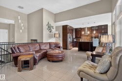Open-concept living area with high ceilings, tile flooring, and a kitchen featuring dark wood cabinetry, a stone-finish backsplash, and stainless steel appliances - 