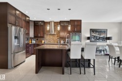 Gourmet kitchen featuring extensive dark wood cabinetry, stainless steel appliances, a stone-finish backsplash, a central island with a countertop, and recessed lighting - 