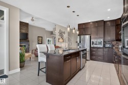 Kitchen island with dark cabinetry and a polished countertop, stainless steel appliances, tiled backsplash, and recessed lighting - 