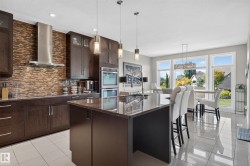 Gourmet kitchen featuring dark wood cabinetry, stainless steel appliances, a large center island with a granite countertop, and a textured backsplash - 