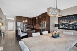 Integrated kitchen and dining area featuring dark wood-finish cabinetry, stainless steel appliances, a kitchen island with seating, a large dining table, and tile flooring - 