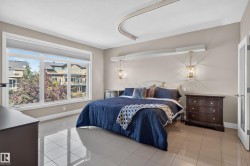 Spacious bedroom featuring large windows, tiled flooring, pendant lighting, and a frosted glass panel door - 