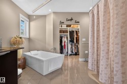 Freestanding soaking tub with chrome fixtures, tiled flooring, built-in shelving, and a patterned privacy curtain - 
