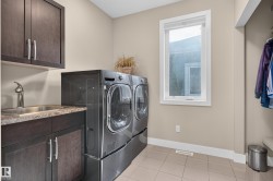 Laundry area with a utility sink, dark wood-finish cabinetry, light-toned tile flooring, and a window - 