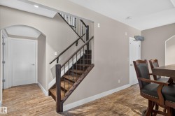 Wood-finish flooring, staircase with dark wood newel posts and railings, wrought iron balusters, recessed lighting, and an arched doorway - 