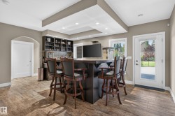 Built-in wet bar with wood-finish flooring, recessed lighting, and a glass-paneled door leading to an outdoor patio - 
