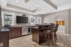 Built-in bar featuring wood cabinetry, granite countertops, an integrated beverage refrigerator, and wood-finish flooring - 