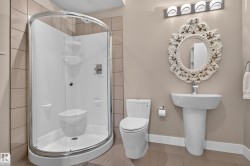 Corner shower enclosure with clear glass, pedestal sink, wall-mounted mirror with decorative frame, and tile flooring - 