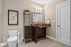 White flat-panel interior door, compact white toilet, wall-mounted vanity with a dark wood-finish base, brown countertop, and a wall-mounted light fixture - 