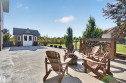 Expansive concrete patio with a detached shed and a built-in wood storage rack, bordered by mature landscaping - 