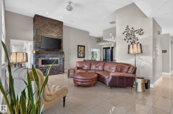 Tiled flooring and vaulted ceilings create an open living space featuring a stacked stone fireplace with a wood mantle and an integrated electric fireplace - 