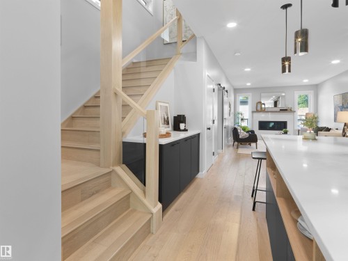 Hardwood flooring throughout, modern staircase with wood and glass railings, built-in cabinetry with a white countertop, recessed lighting, and a linear electric fireplace - 9118 89 Street Nw, Edmonton, AB 