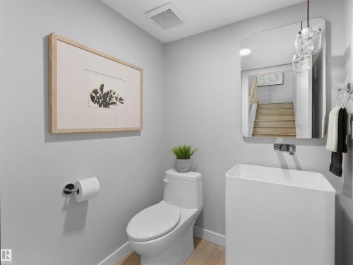 Compact powder room featuring a white pedestal sink, wall-mounted faucet, and light wood-finish flooring - 9118 89 Street Nw, Edmonton, AB 