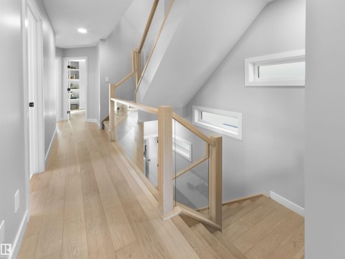 Light wood-finish flooring extending throughout, contemporary glass and wood staircase, recessed lighting, white trim, and built-in shelving - 9118 89 Street Nw, Edmonton, AB 