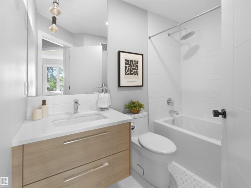 Bathroom featuring a wood-finish vanity with an integrated sink, a white countertop, a mirror, and a tiled bathtub with a shower - 9118 89 Street Nw, Edmonton, AB 