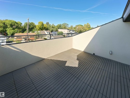 Rooftop patio featuring composite decking, a stucco privacy wall, and a black metal railing - 9118 89 Street Nw, Edmonton, AB 