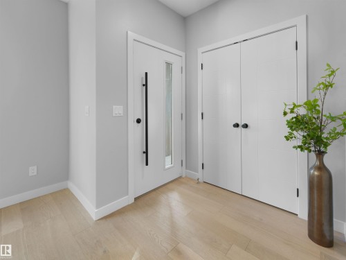 Entryway featuring light wood-finish flooring, white walls, and a white front door with a vertical glass insert and a black handle - 9118 89 Street Nw, Edmonton, AB 